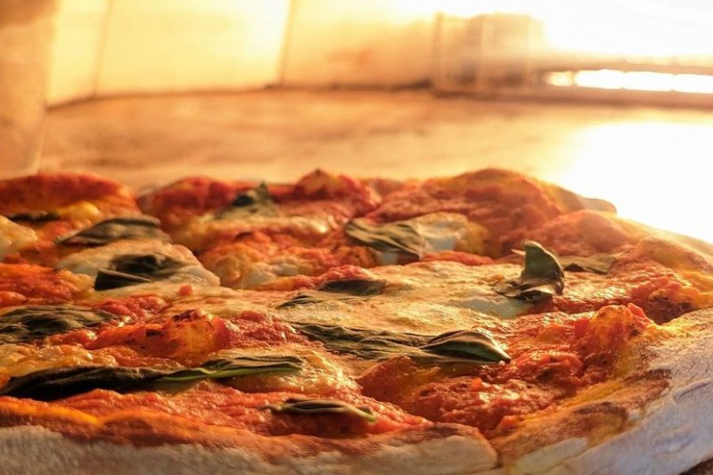 Golfplay A close-up of a Margherita pizza baking in a wood-fired oven at Golfplay, with melted cheese, tomato sauce, and basil leaves visible—perfect for enjoying after a session at the golf simulator. Indoor Golf