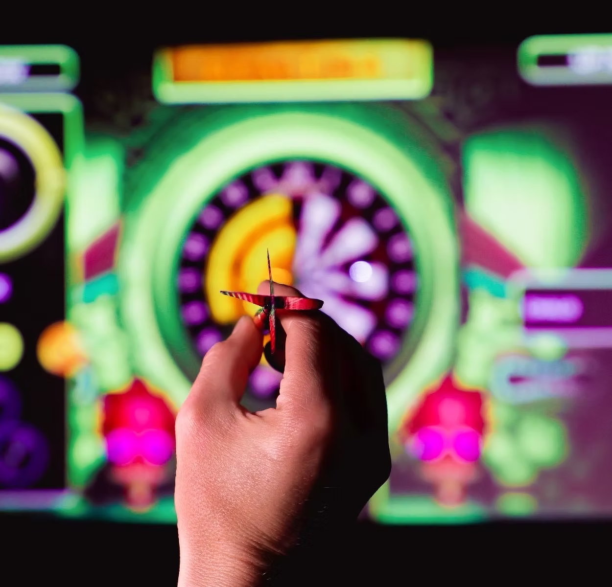 Golfplay A hand holding a dart is aimed at an electronic dartboard with bright, colorful digital graphics in the background, capturing the excitement found in Golfplay indoor golf and golf simulator experiences. Indoor Golf