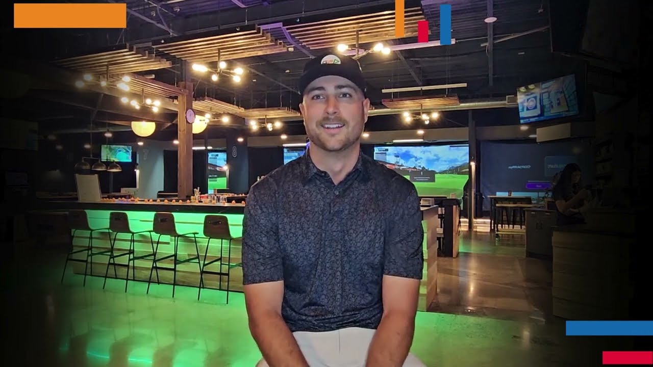 Golfplay A man in a golf cap and polo shirt sits indoors at a Golf Simulator venue with bar seating, neon lighting, and large screens in the background. Indoor Golf