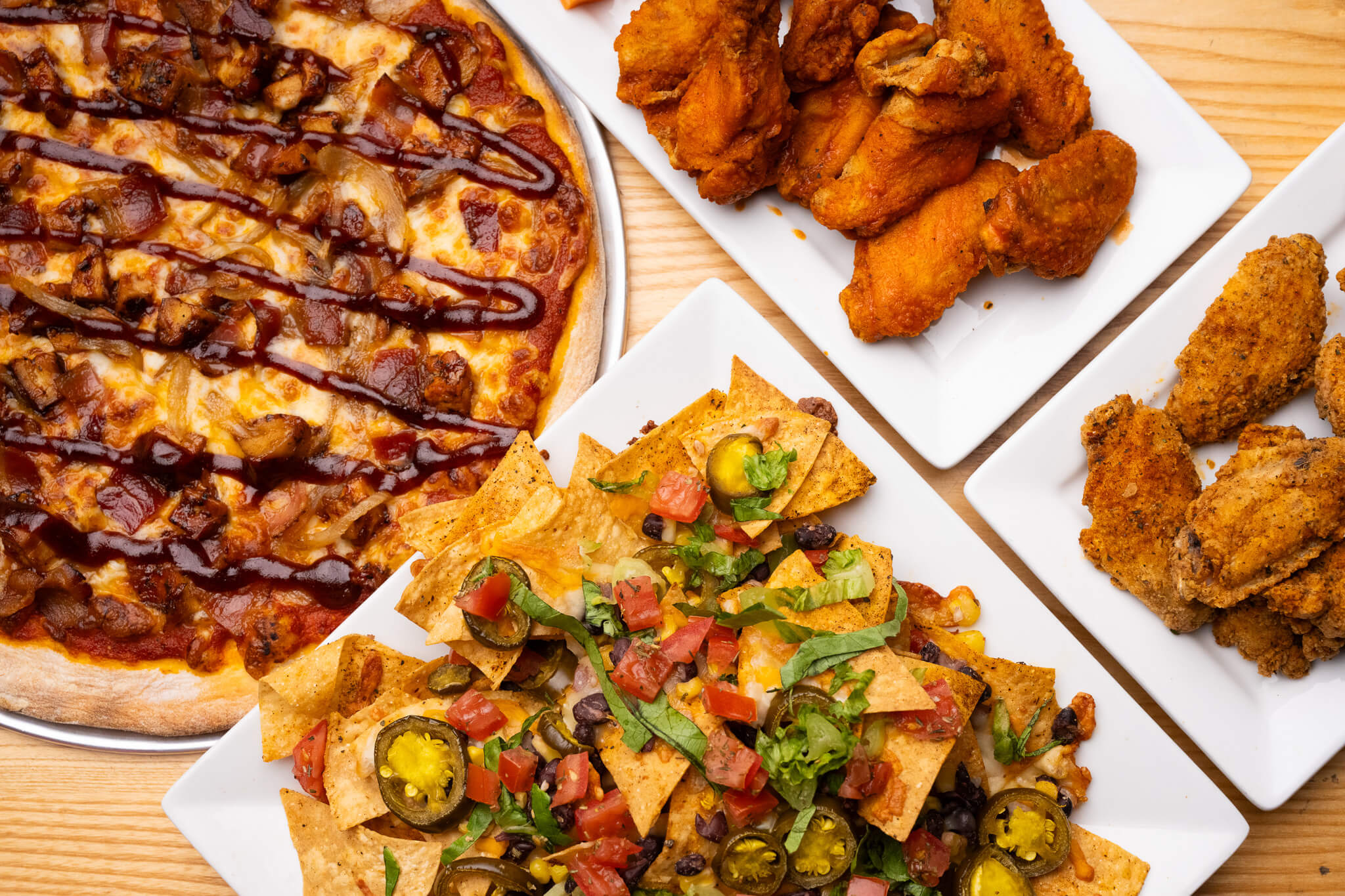 Golfplay A table at Golfplay features barbecue chicken pizza, nachos topped with vegetables and jalapenos, and plates of fried and breaded chicken wings—perfect for enjoying between rounds on the indoor golf simulator. Indoor Golf