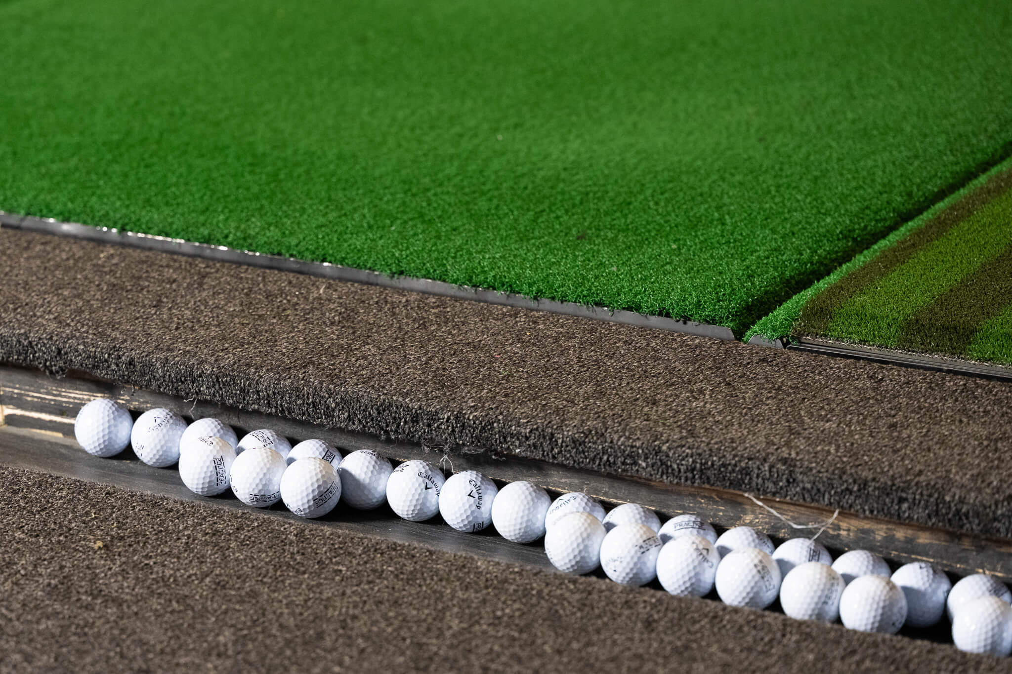 Golfplay A row of white golf balls lined up in a groove on an artificial turf mat at an Indoor Golf driving range. Indoor Golf