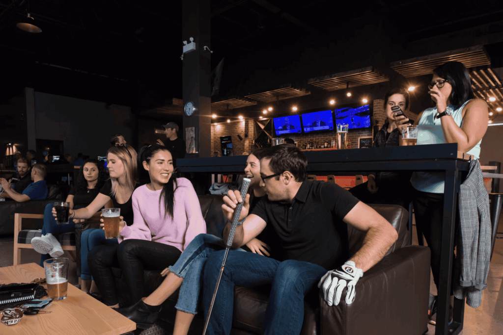 Golfplay A group of people sitting on a couch, relaxing together after an exciting round using the indoor golf simulator. Indoor Golf